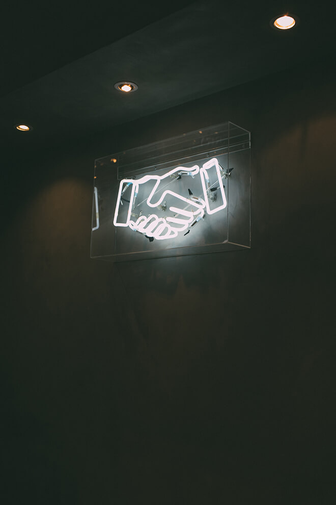 A neon sign of a handshake hung upon the wall